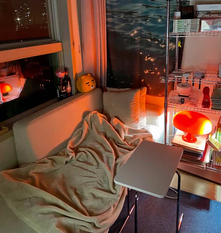 Living room by window in white and red light tones featuring a cozy sofa with blanket, side table, and floor lamp