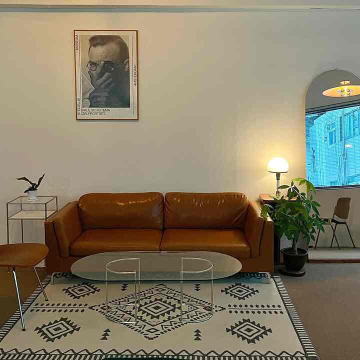 A natural-toned living room featuring a brown leather sofa, geometric patterned rug, and an arched mirror with a simple modern atmosphere