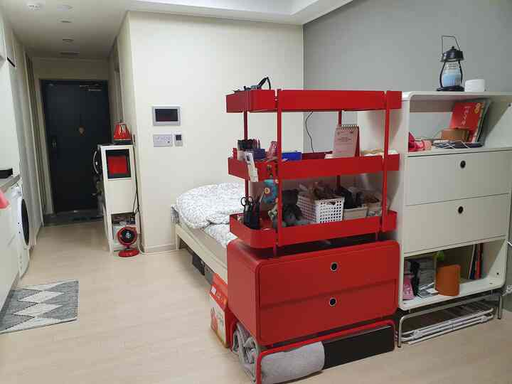 A narrow bedroom with white background and red shelving unit, featuring minimal storage ideas and a cozy atmosphere