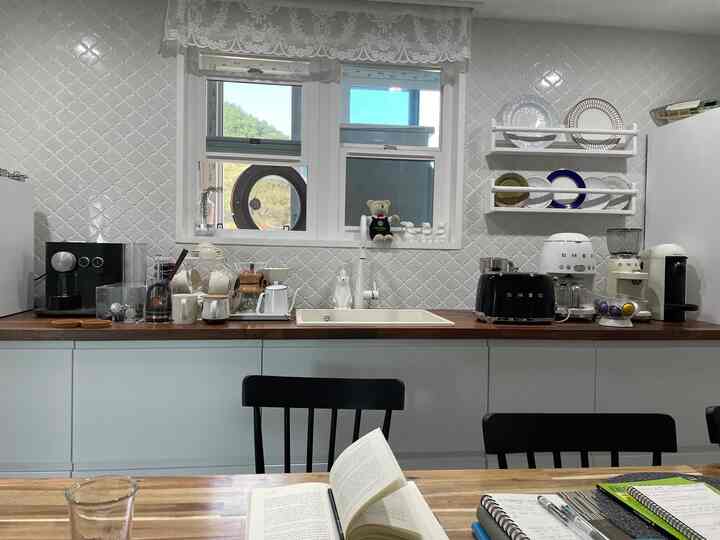 白いタイル壁と木目調のカウンターが調和するキッチン、さまざまなコーヒー器具とデスクが配置された雰囲気のあるおうちカフェ空間