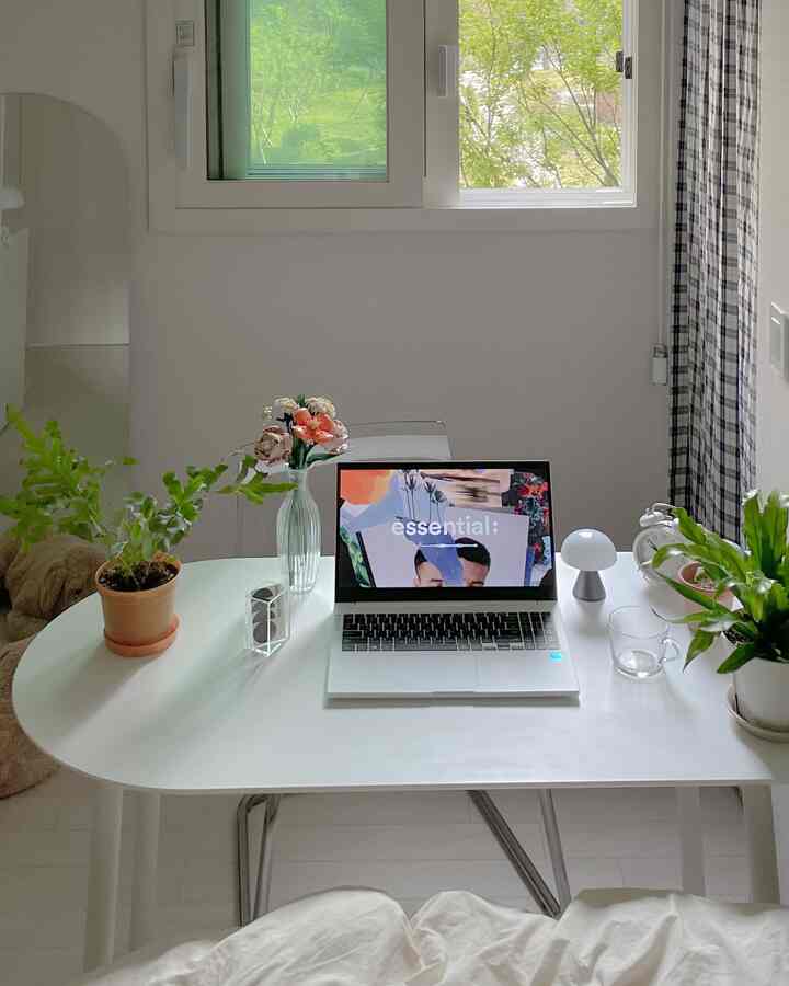 White-toned bedroom home office with natural plants on desk, featuring a laptop in a simple and minimal setting