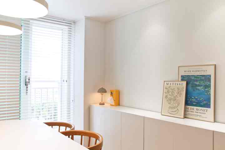 White and wood-toned dining room featuring a clean dining table, chairs, and framed posters, creating a cozy space