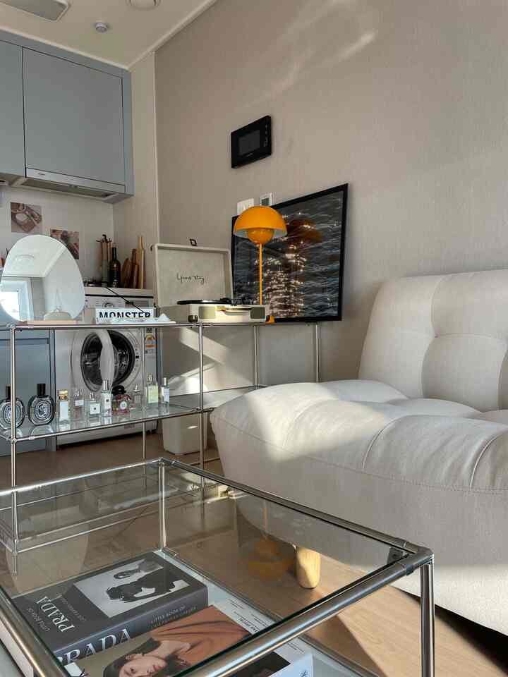 Natural tone living room featuring a white sofa, glass coffee table, and orange table lamp creating a cozy atmosphere