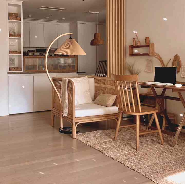 ナチュラルな色調のリビングルームのホームオフィス、ラタンソファと木製デスク・チェア、プリーツ照明が置かれた雰囲気のあるインテリア