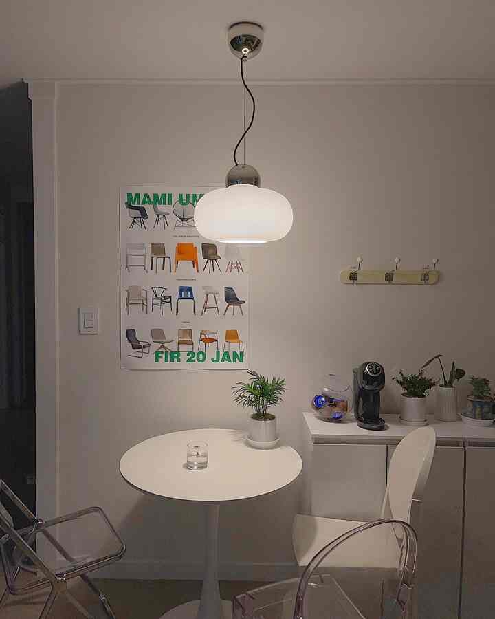 A modern compact home cafe dining area in white tones featuring transparent chairs and a pendant light
