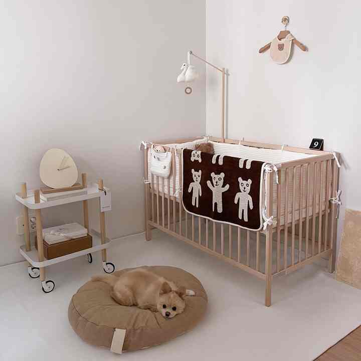 White and beige toned baby room featuring a wooden crib and beige pet bed creating a cozy atmosphere