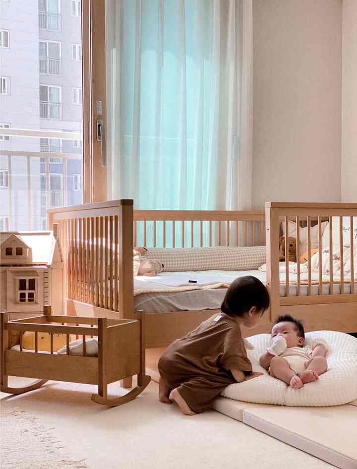 暖かみのある木目調と白の子供部屋、ベビーベッドと子供用ベッドが配置された居心地の良い空間