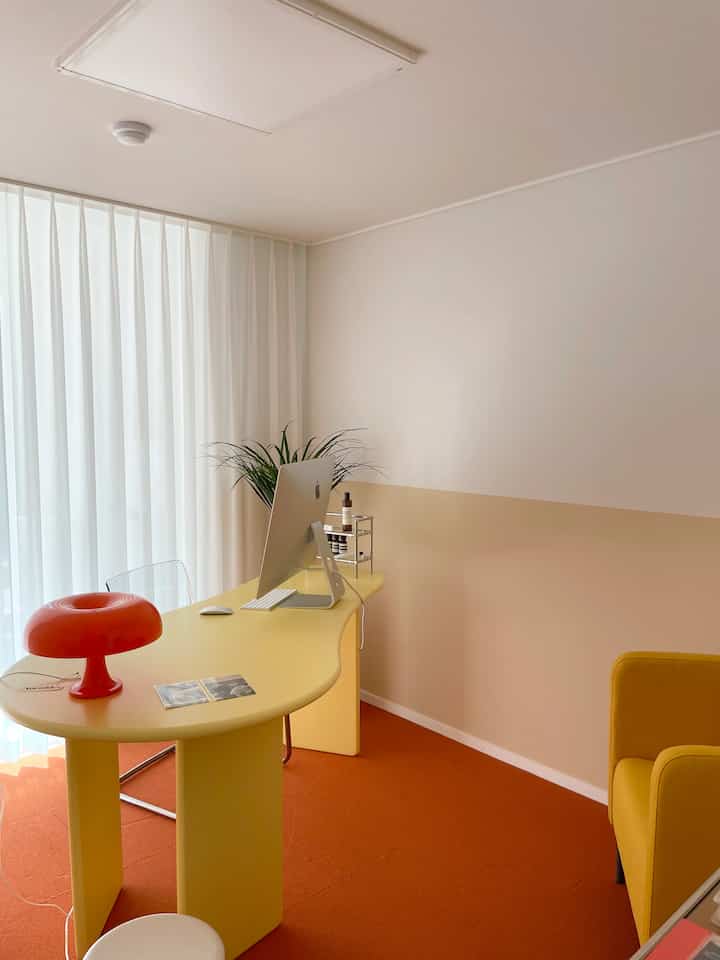 Yellow and orange toned study featuring a curved desk, sheer curtains, and a yellow armchair with warm, bright ambiance