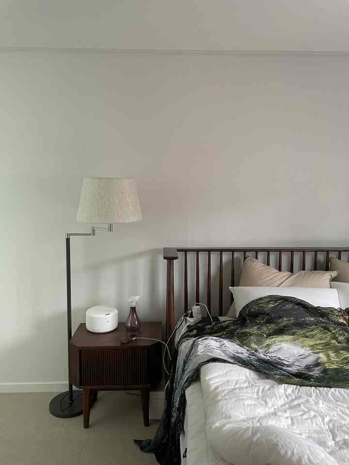 白い壁と茶色の木製家具が調和した寝室、整ったベッドとフロアランプが配置された落ち着いた雰囲気のインテリア