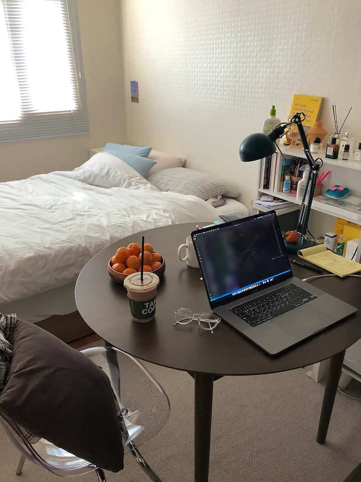 白と茶色のトーンのワンルーム、丸テーブルとベッドが配置された落ち着きのある実用的な初めての一人暮らしの部屋