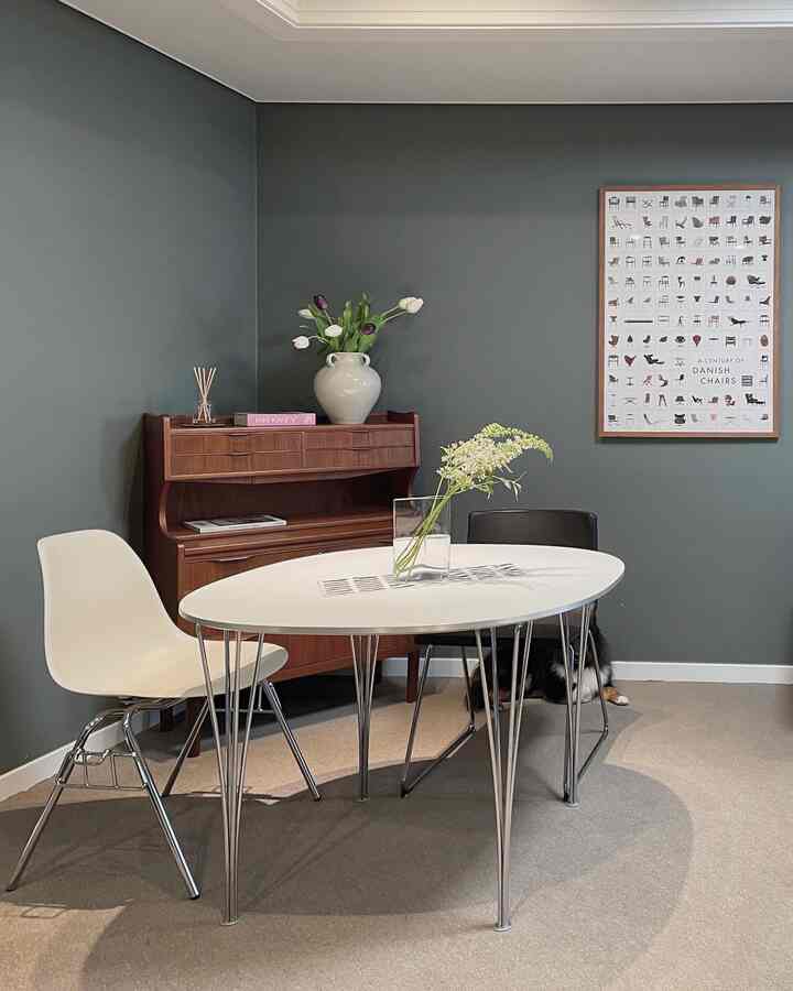 Contemporary dining area with dark gray walls, mid-century modern wood-tone sideboard, white oval dining table and chairs, featuring a dog resting in the corner