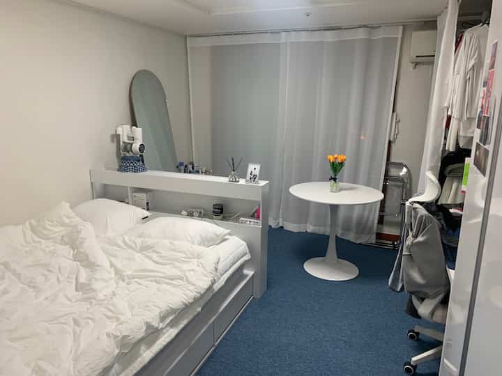 ホワイトとブルーのトーンの小さな寝室、ベッドと丸テーブル、カーテンが配置されたシンプルモダンなインテリア