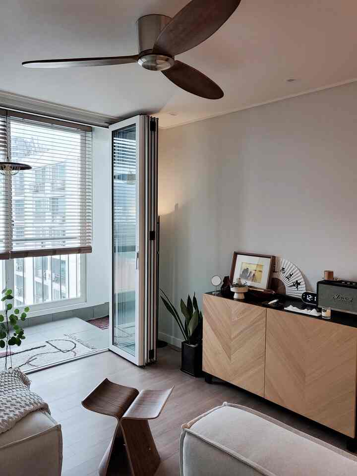 Natural wood tone living room featuring large windows with wooden blinds, folding glass door, cozy sofa, and minimalist furniture layout creating a warm atmosphere