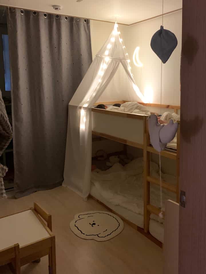 ナチュラルな木目調と白い灯りが印象的な子供部屋、二段ベッドとカーテンが配置された温かみのあるインテリア