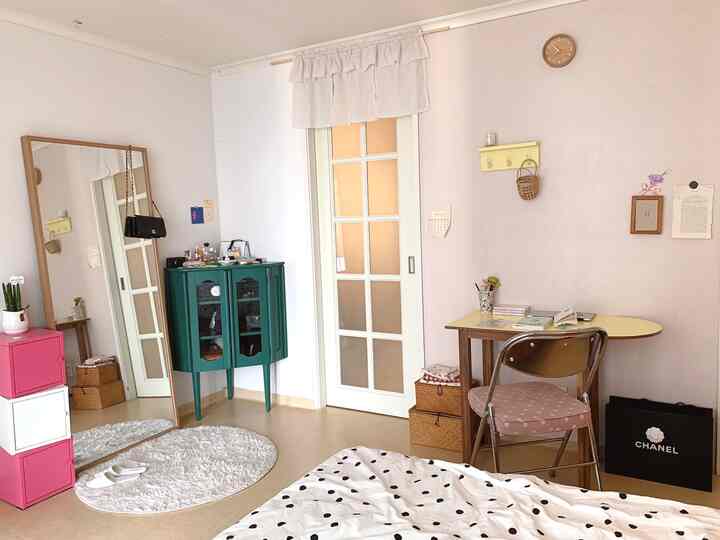 ホワイトとピンクのトーンが調和した寝室、グリーンのコーナー収納とデスクが配置された雰囲気のある空間