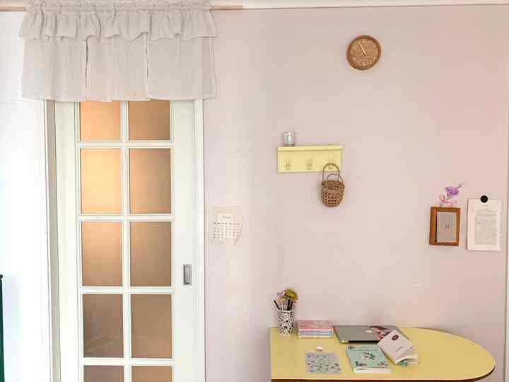 A compact bedroom study with white walls and curtains, featuring a yellow desk and mid-century modern style elements