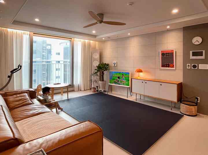 Bright white and brown toned living room featuring large window, sofa, and child's chair in a modern, tidy space