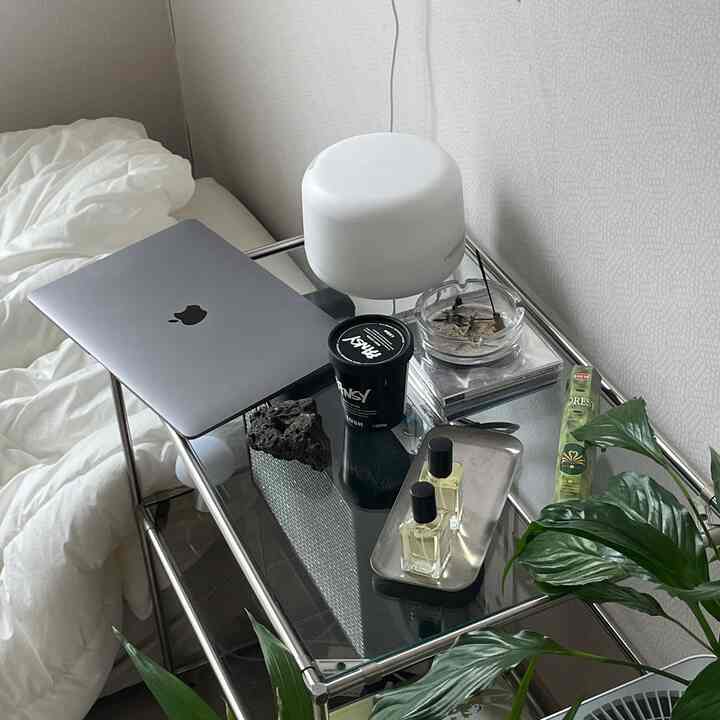 白を基調とした寝室、ステンレスのナイトテーブルにノートパソコンやディフューザー、香水瓶が整然と配置されたモダンなインテリア