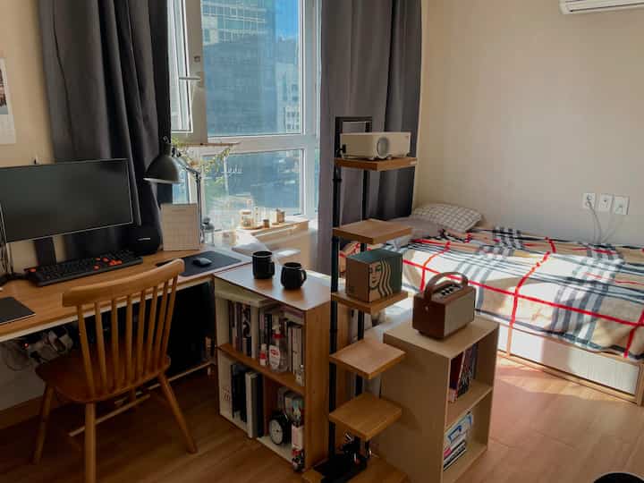 Brown and gray toned studio bedroom featuring desk, bookshelf, and blackout curtains with a warm and cozy atmosphere