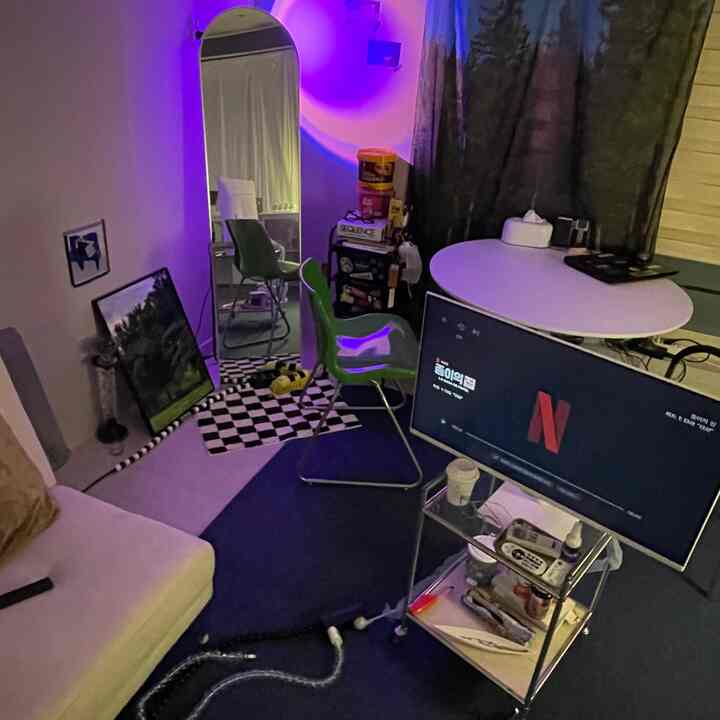 青い照明が印象的なリビング、ホワイトソファとグリーンチェア、テレビ台が配置されたモダンなインテリア