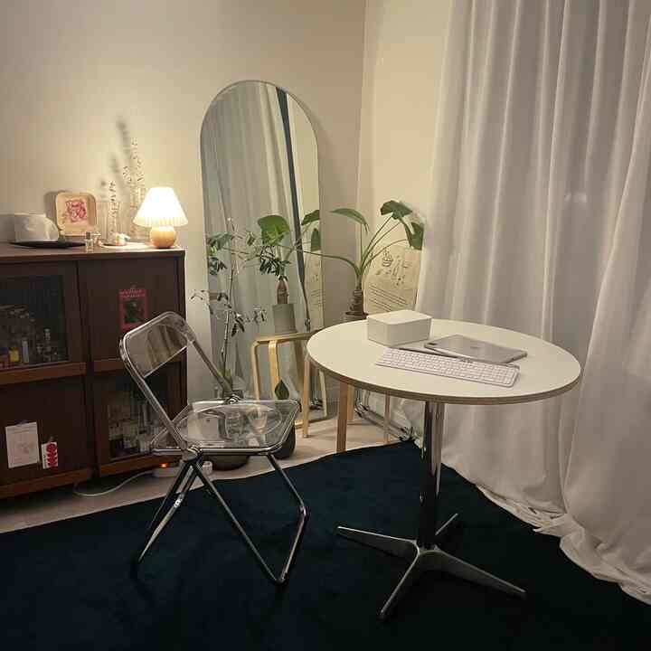 白と黒のトーンの円形の部屋、透明な折りたたみ椅子と丸テーブル、植物が配置されたミッドセンチュリーモダンのホームオフィス空間