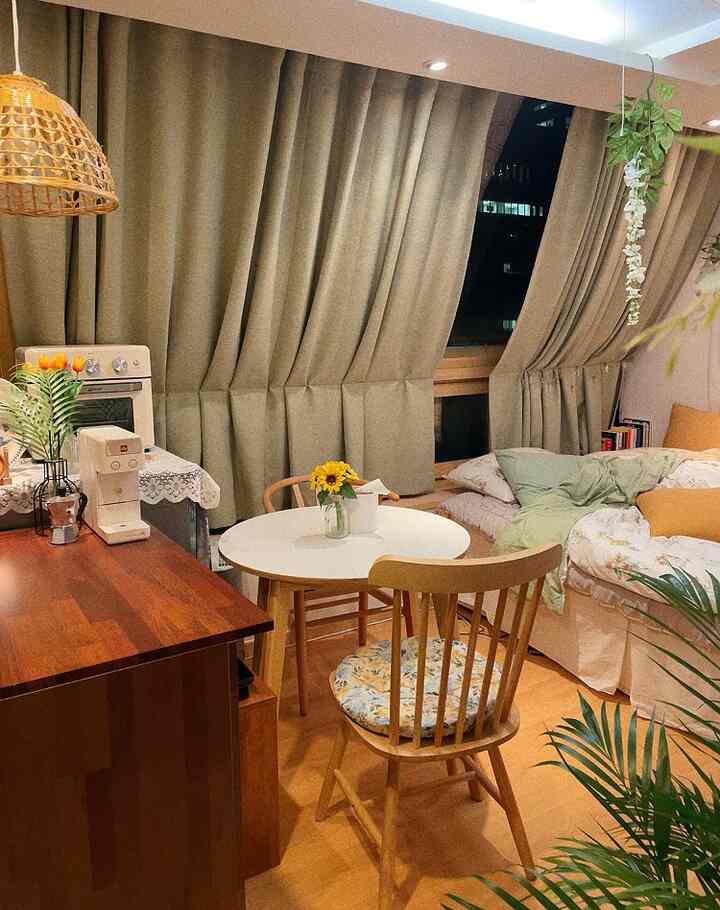 Beige and natural tone studio apartment featuring wooden dining table and chairs, bedding, blackout curtains, and rattan pendant light creating a cozy interior
