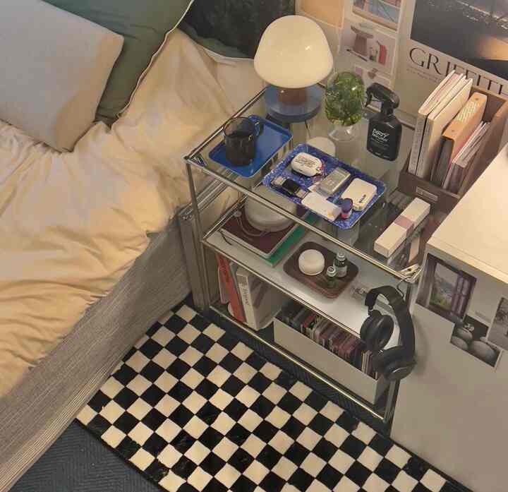 Natural-toned bedroom featuring bed with pillows and a glass nightstand holding various items, creating a cozy atmosphere