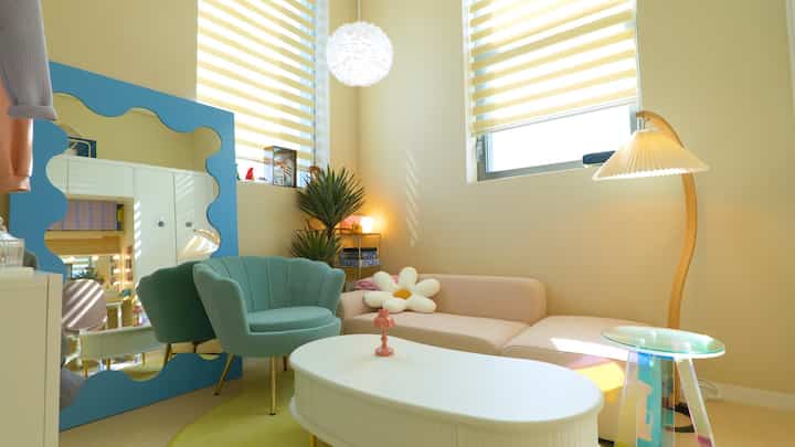 Loft living room with pale yellow walls, pink sofa, and mint armchair, brightened by natural light creating cozy atmosphere
