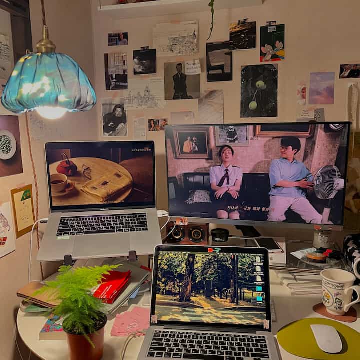 White-toned home office space featuring three computers, wall decor, and a plant creating a cozy workspace