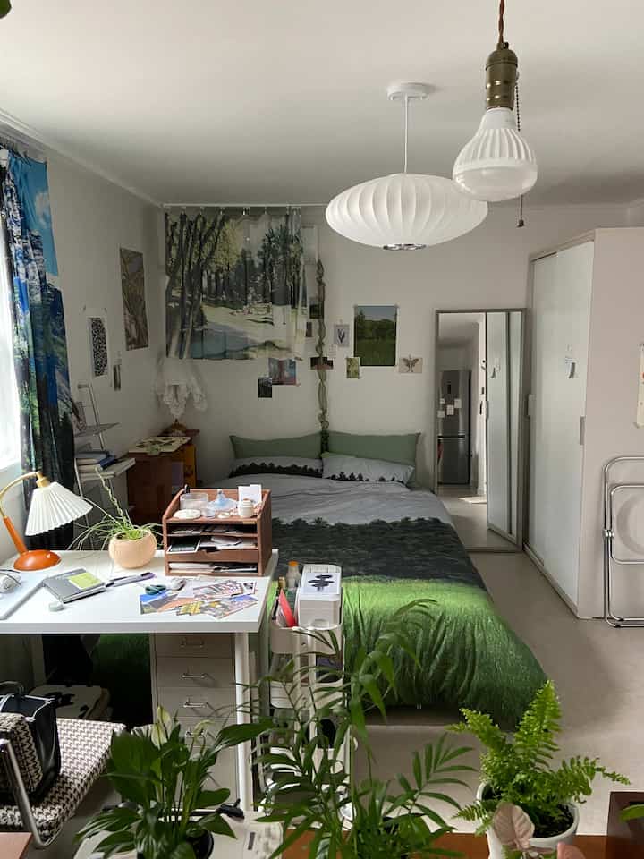 White and green toned studio bedroom featuring nature-themed bedding and plants creating a natural ambiance