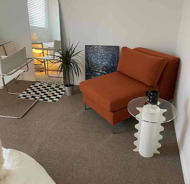 白い壁とシンプルモダンスタイルのオレンジのひとり掛けソファ、サイドテーブル、鏡、植物が配置されたリビング