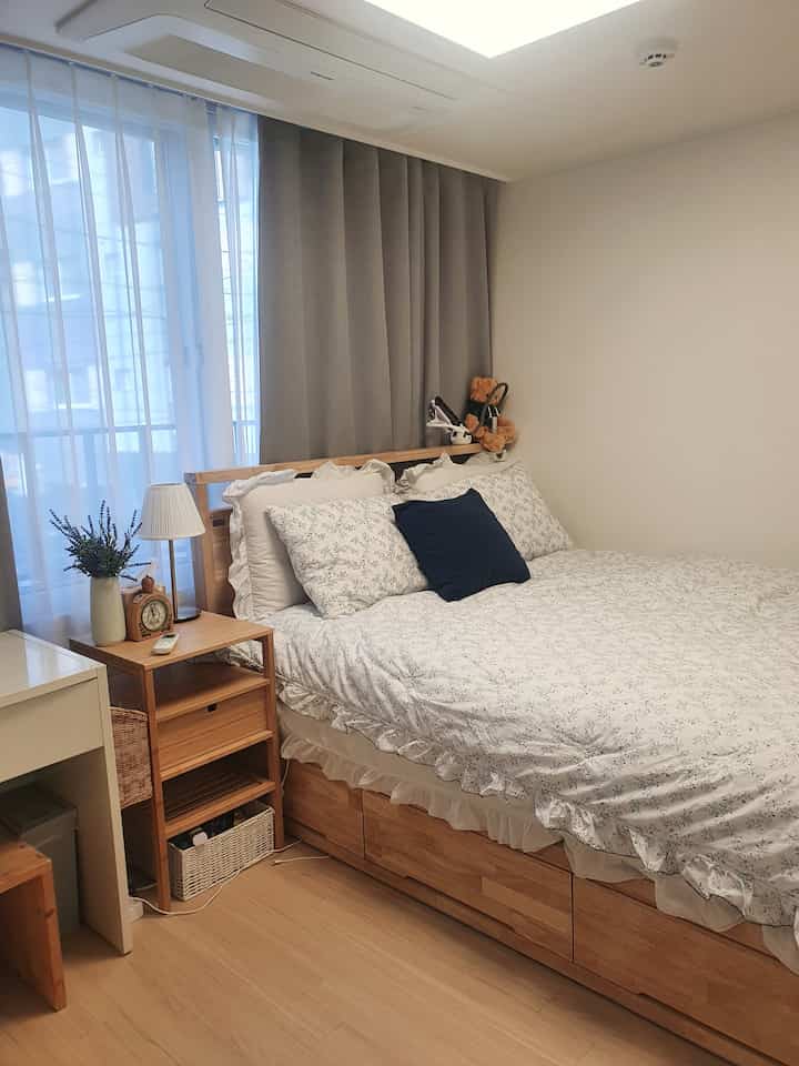 ホワイトとウッドトーンが調和した寝室、花柄寝具と収納付きベッドが配置された居心地の良い小さな部屋