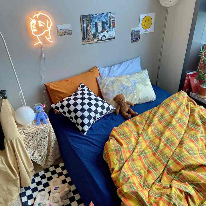 Yellow and navy toned bedroom featuring a bed with checkered pillow and teddy bear, complemented by neon wall light and mood lamp for cozy atmosphere
