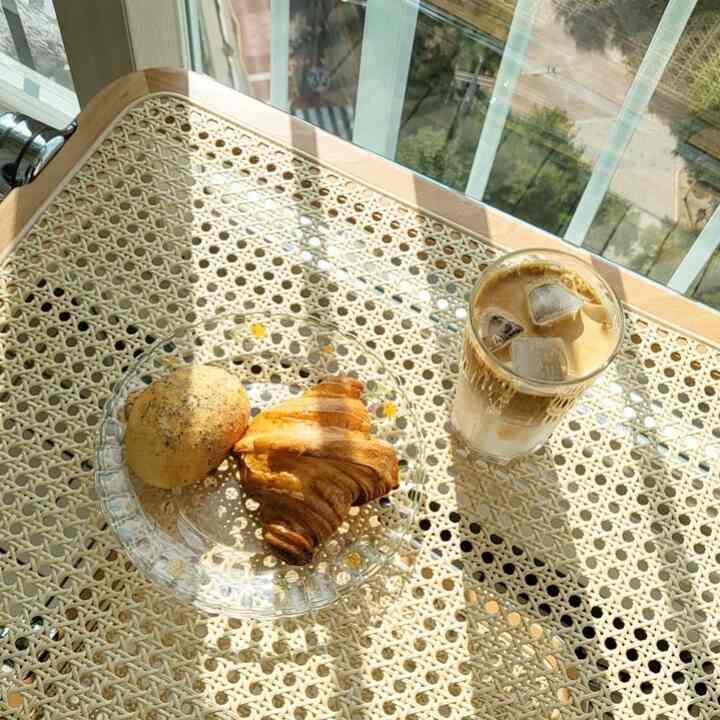 陽光が差し込むラタンテーブルの上にガラス皿とアイスコーヒーが置かれた雰囲気のあるおうちカフェ