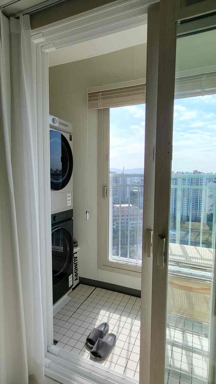 明るいホワイトトーンのバルコニー、木製ブラインドと洗濯機が配置された清潔感のあるランドリースペース