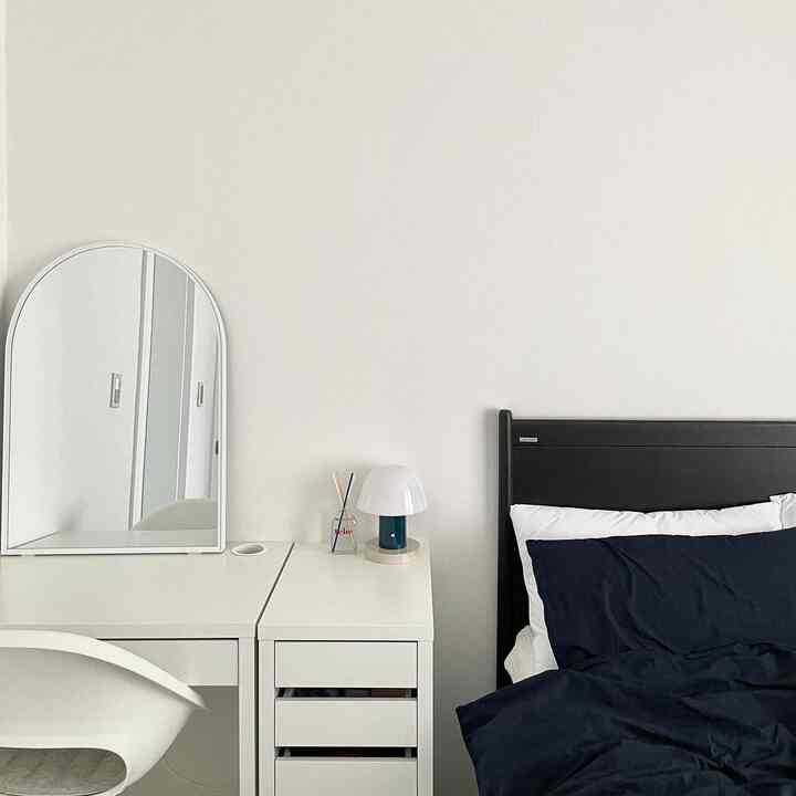 ホワイトとブラックを基調とした寝室、デスクにアーチ形の鏡とネイビーの寝具が配置されたモダンなインテリア