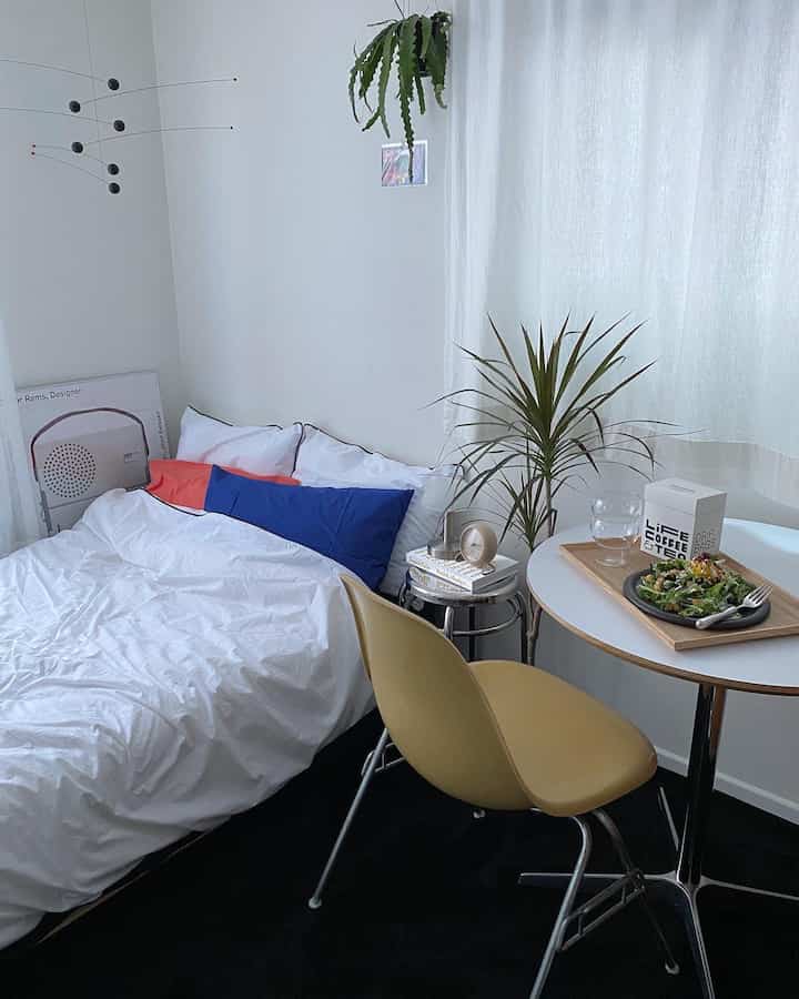 White and black toned studio bedroom featuring a round table, Eames chair, and green plants creating a minimal home cafe atmosphere