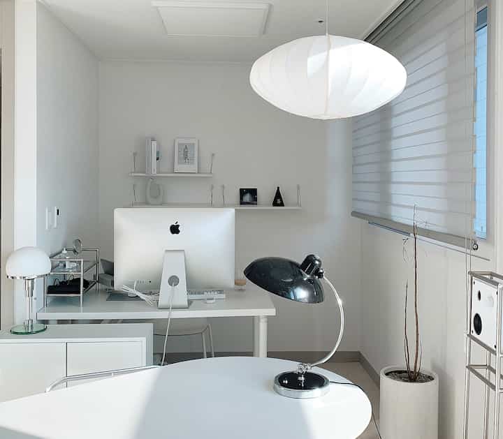 Bright white-toned clean home office space featuring a white desk and a black desk lamp in a modern workspace