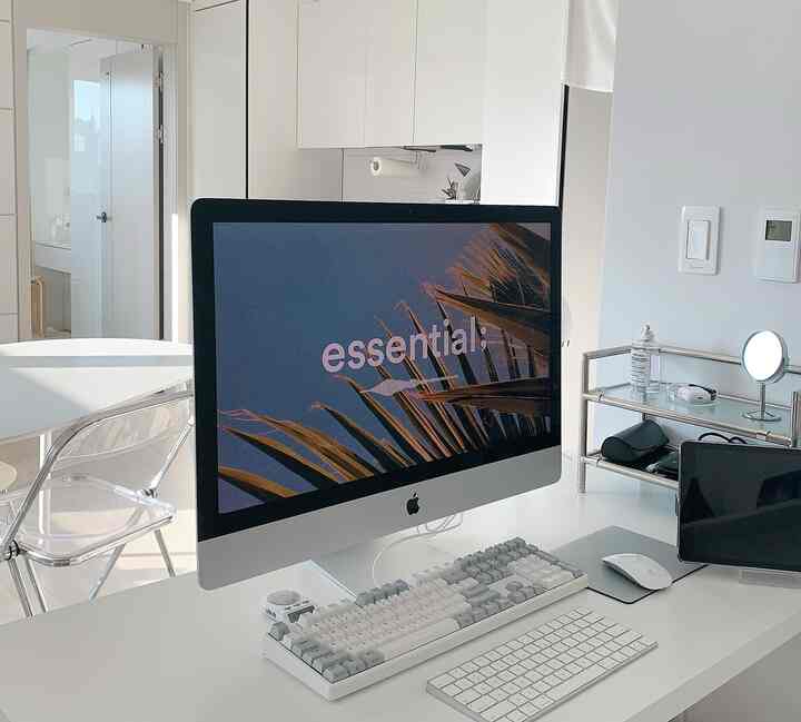 White-toned home office space featuring transparent chair and iMac computer; clean and modern interior