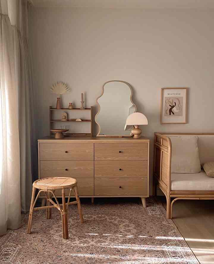 A natural bedroom featuring soft wood tones and beige curtains, centered with a unique irregular mirror and dresser