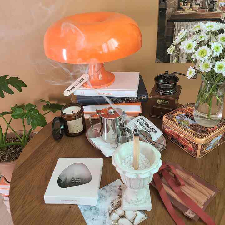 Warm orange and wood tones feature a round table with Artemide Nessino lamp, candles, and palo santo incense in a natural vintage style studio space