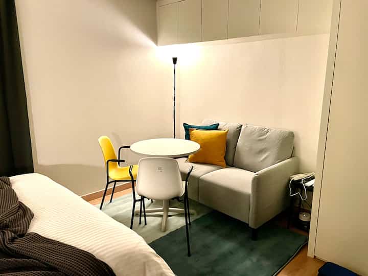 White and gray toned studio bedroom featuring a sofa and round dining table with a hotel-like style