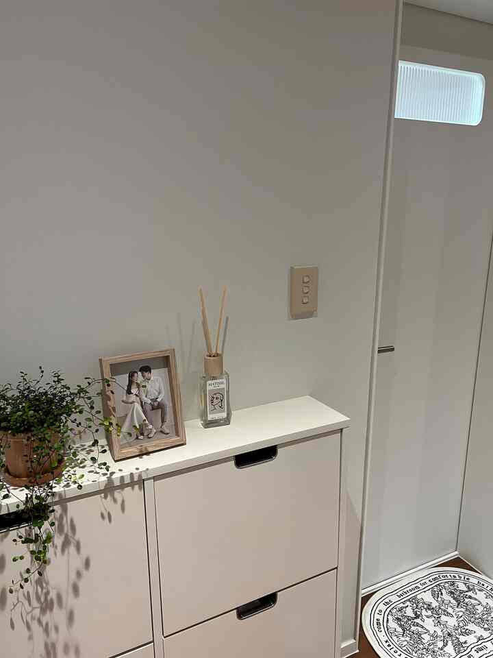 A hallway apartment storage cabinet with white walls, wooden picture frame, and diffuser creates a clean and natural atmosphere