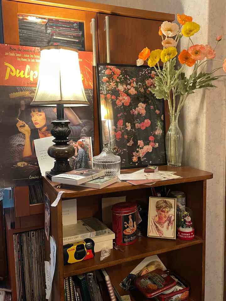 Warm wood tone vintage-style room featuring classic posters, vase with colorful flowers, and stand lamp creating a cozy atmosphere