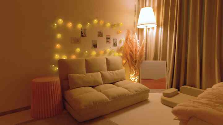 Warm beige-toned living room featuring a beige sofa bed, blackout curtains, and decorative lighting creating a cozy atmosphere