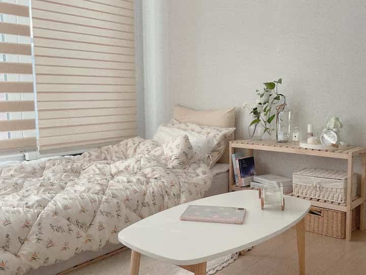 Cozy beige-toned bedroom featuring patterned bedding, wooden shelving, and plants creating a natural atmosphere