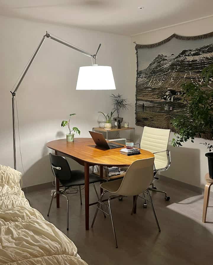 白い壁と茶色い木製のダイニングテーブルと椅子が配置されたミッドセンチュリーモダン風のワンルームリビングスペース