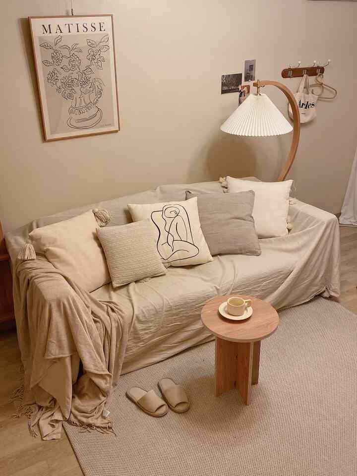 Beige and wood tone living room featuring beige sofa with cushions, rug, round wooden side table, and floor lamp in a natural and simple setting