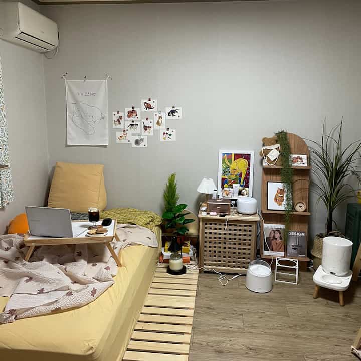 Beige and wood tone bedroom featuring wooden furniture, artificial plants, and a cozy home cafe vibe with tray and coffee on bed