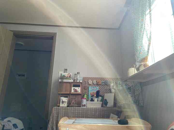 ベージュと木目調の狭いワンルーム、中央にノートパソコンが置かれた木製トレイと収納棚が配置された落ち着いた作業空間